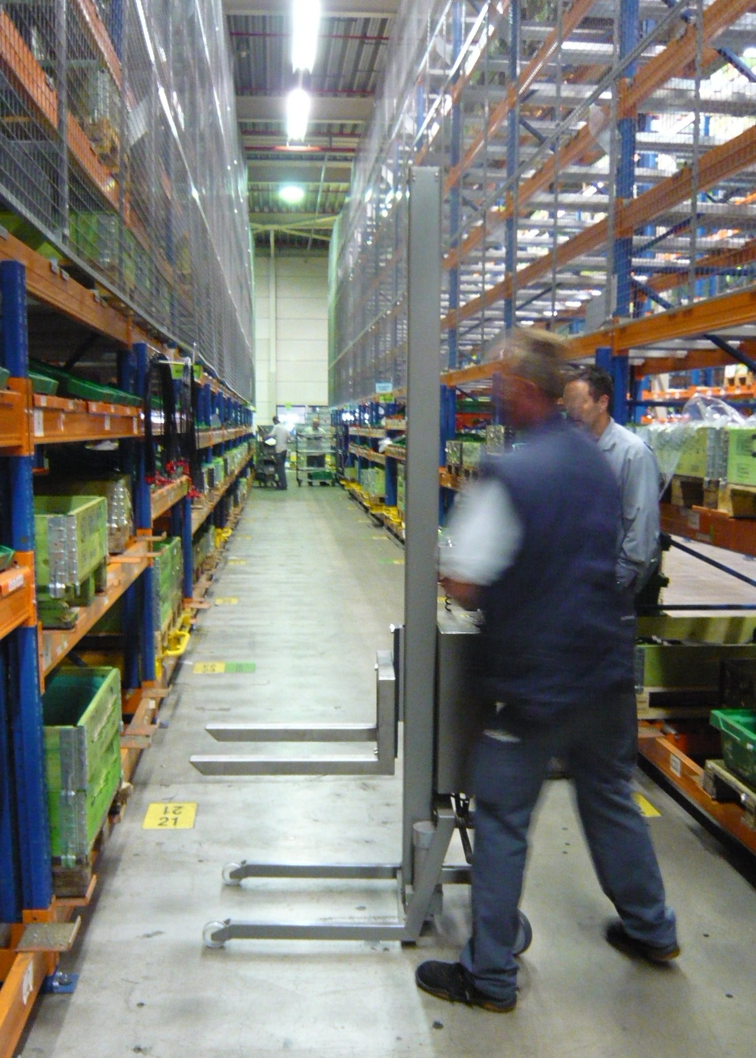 Two workers in a warehouse with high shelves and storage racks.